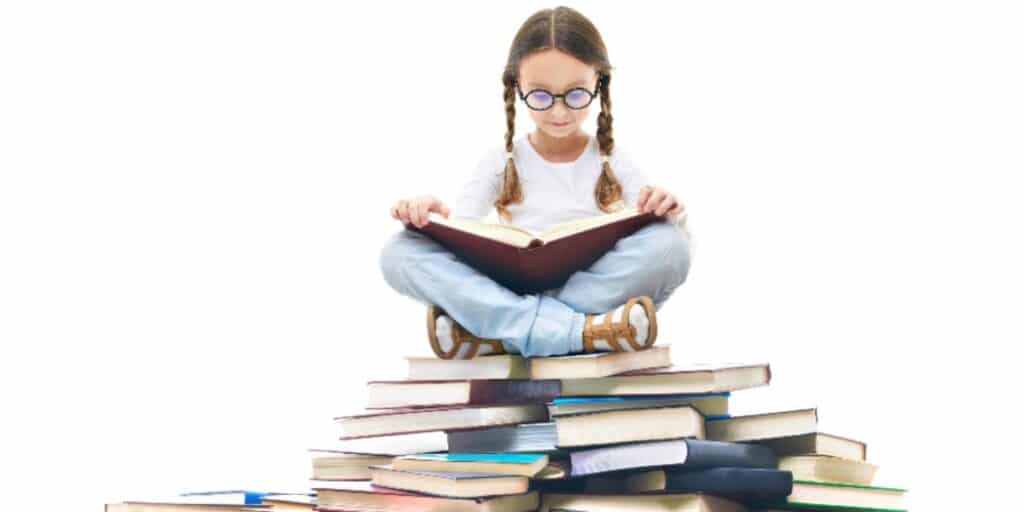 A picture of a young girl sitting atop a large pile of books with an open book on her lap to represent tips for improving your literature survey