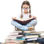 A picture of a young girl sitting atop a large pile of books with an open book on her lap to represent tips for improving your literature survey