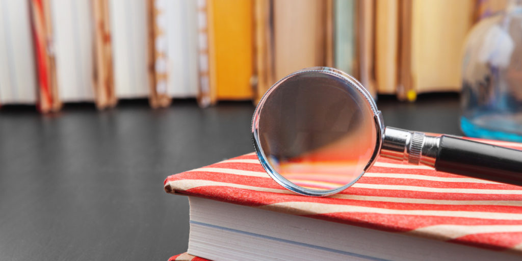 Magnifying glass on a book, symbolizing how a DOI allows doucments to be found