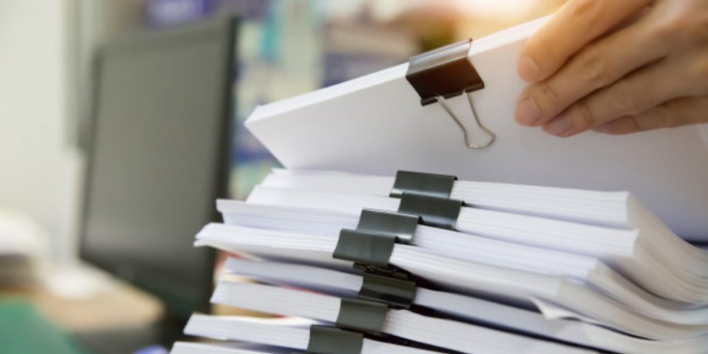 A hand reaches for a stack of paper contained with a binder clip