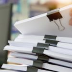 A hand reaches for a stack of paper contained with a binder clip