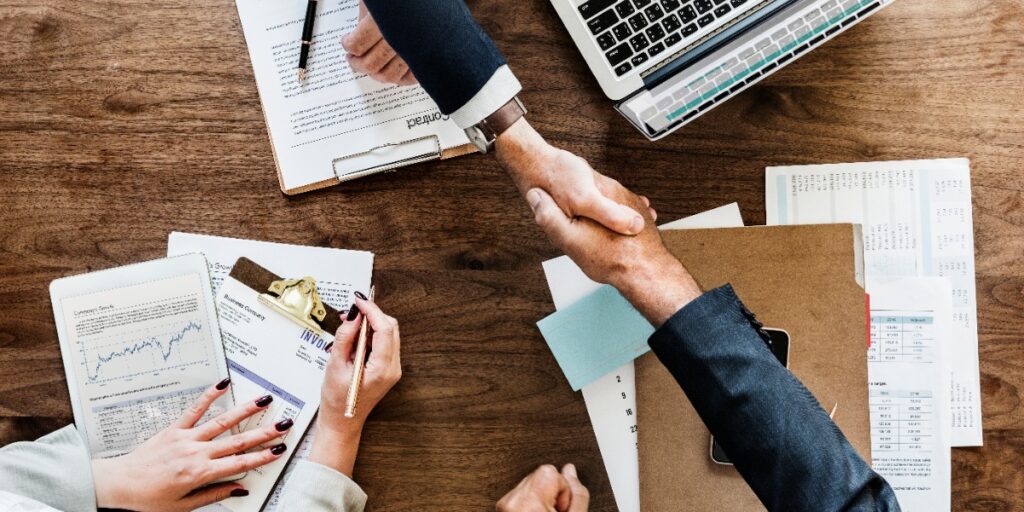 Two people shaking hands over a table, with a third person involved in the meeting, possibly having had a resolution meeting as a strategy for dealing with a difficult lab supervisor.