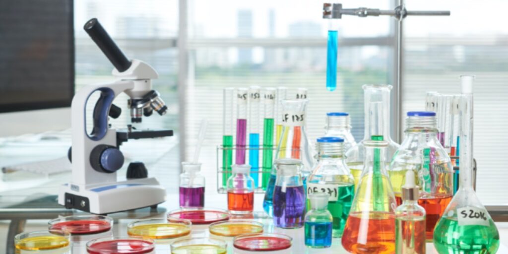 Lab bench with microscope and lots of different coloured reagents in flasks and test tubes to represent someone performing successful experiments