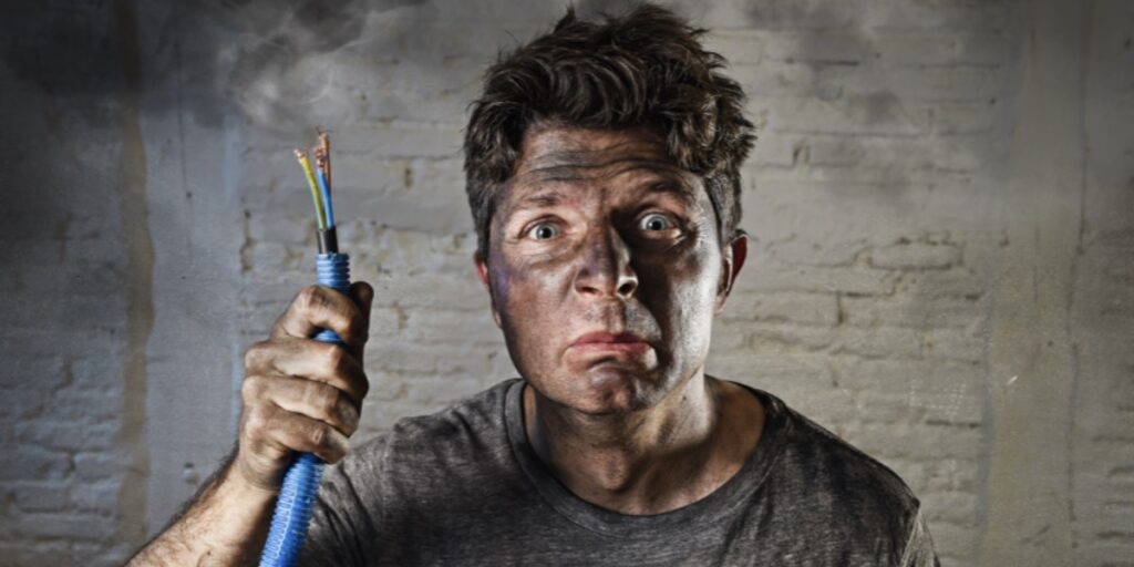 An unhappy looking man covered in soot and holding a cable with exposed wires to represent choosing between constant current or voltage in SDS-PAGE