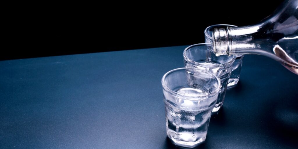 Three shot glasses and a clear glass bottle containing clear alcoholic liquid to represent the ethanol grades that can be used in the lab