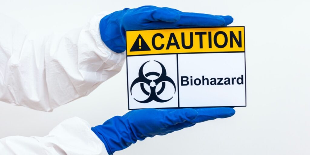 An image of a person's arms in a hazmat suit holding a biohazard warning sign to represent common lab safety signs