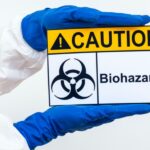 An image of a person's arms in a hazmat suit holding a biohazard warning sign to represent common lab safety signs