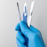 A hand in rubber gloves holding a selection of scalpels for performing various DNA gel extraction methods.