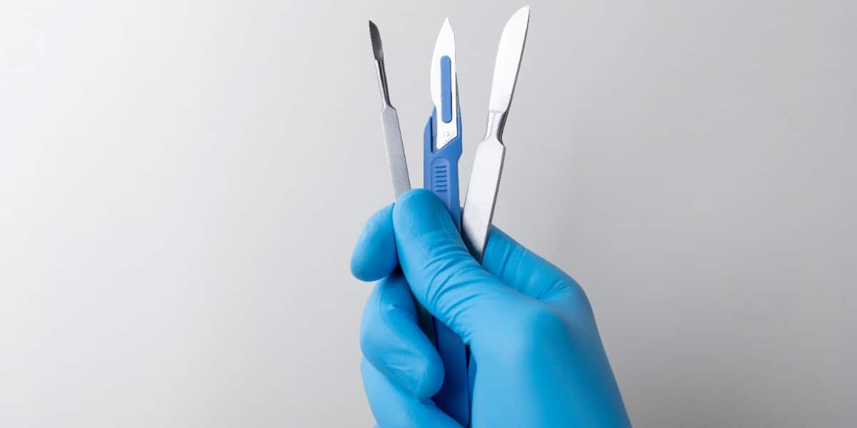 A hand in rubber gloves holding a selection of scalpels for performing various DNA gel extraction methods.